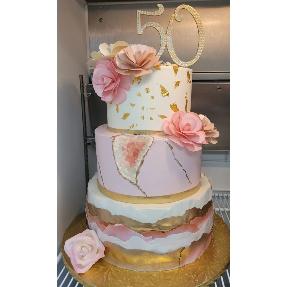 A tiered pink, white and gold cake with sugar flowers